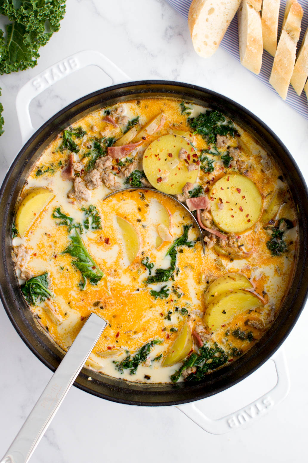 A white pot of zuppa toscana on a marble background.