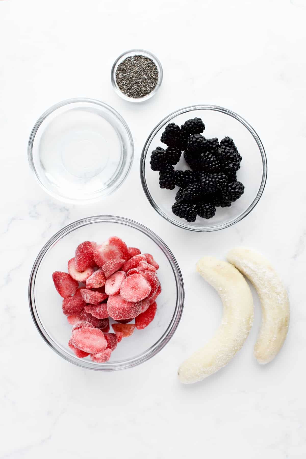 Ingredients for blackberry strawberry banana smoothie on a marble background.