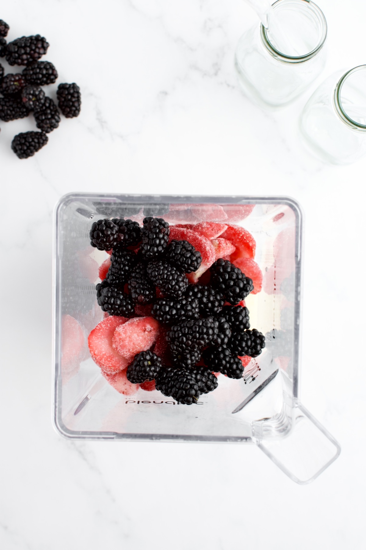 A top down shot of the inside of a blender with fresh blackberries and frozen strawberries, not yet blended.