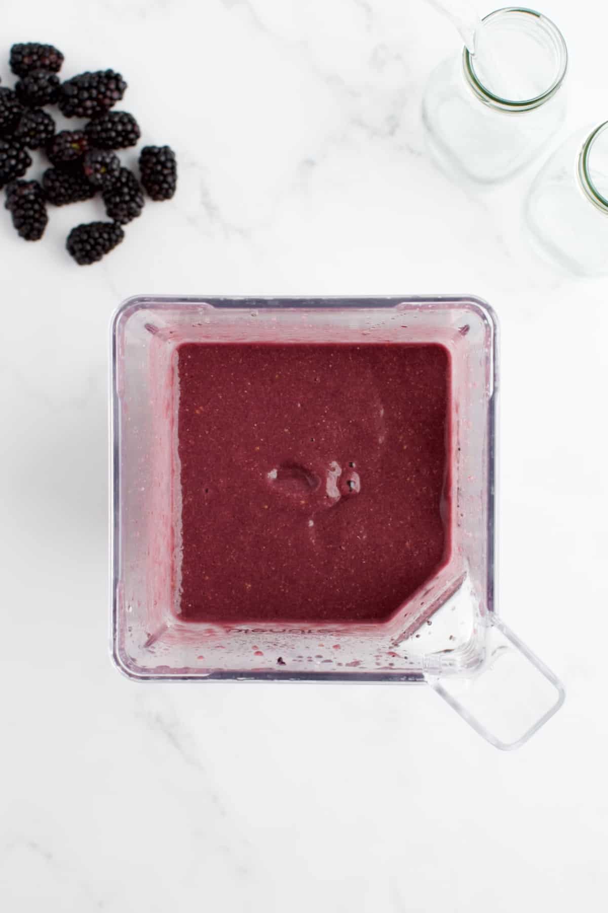 A top down shot of the inside of a blender with blended creamy blackberry strawberry banana smoothie.