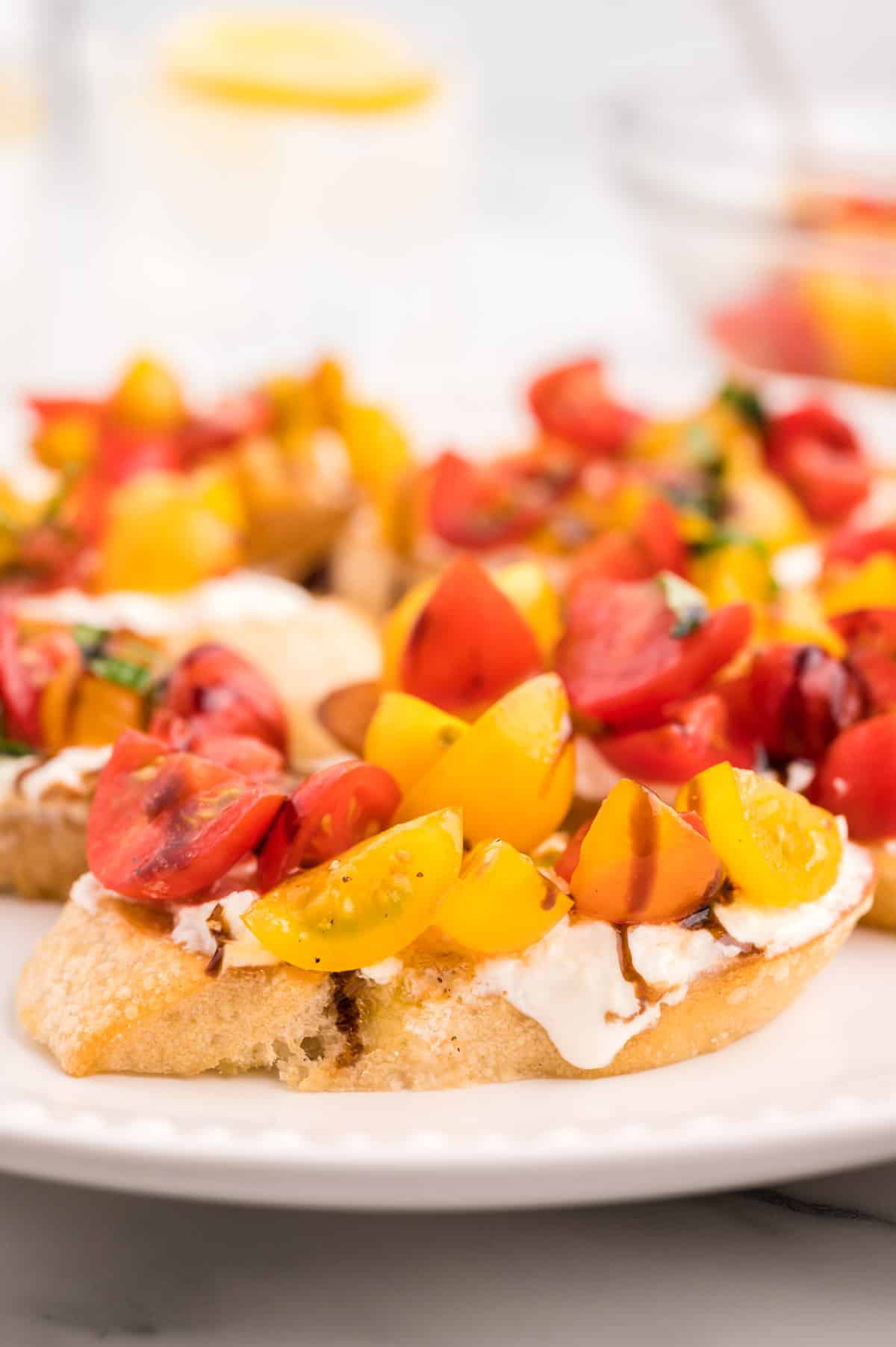 A close up side view of a burrata bruschetta, with more bruschetta blurred in the background.