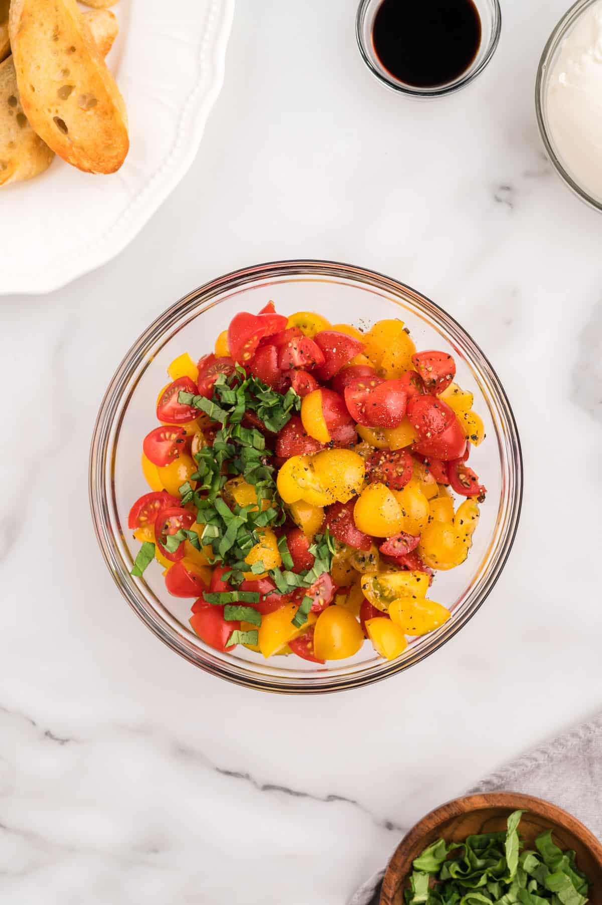 A bowl of cherry tomatoes, with salt and pepper and basil to be mixed in.