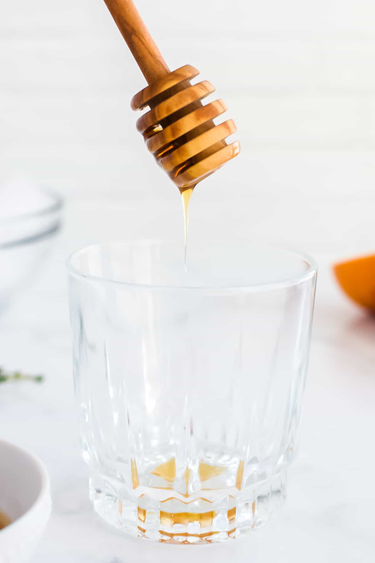 An empty rocks glass on a marble background with a honey spoon drizzling in honey.