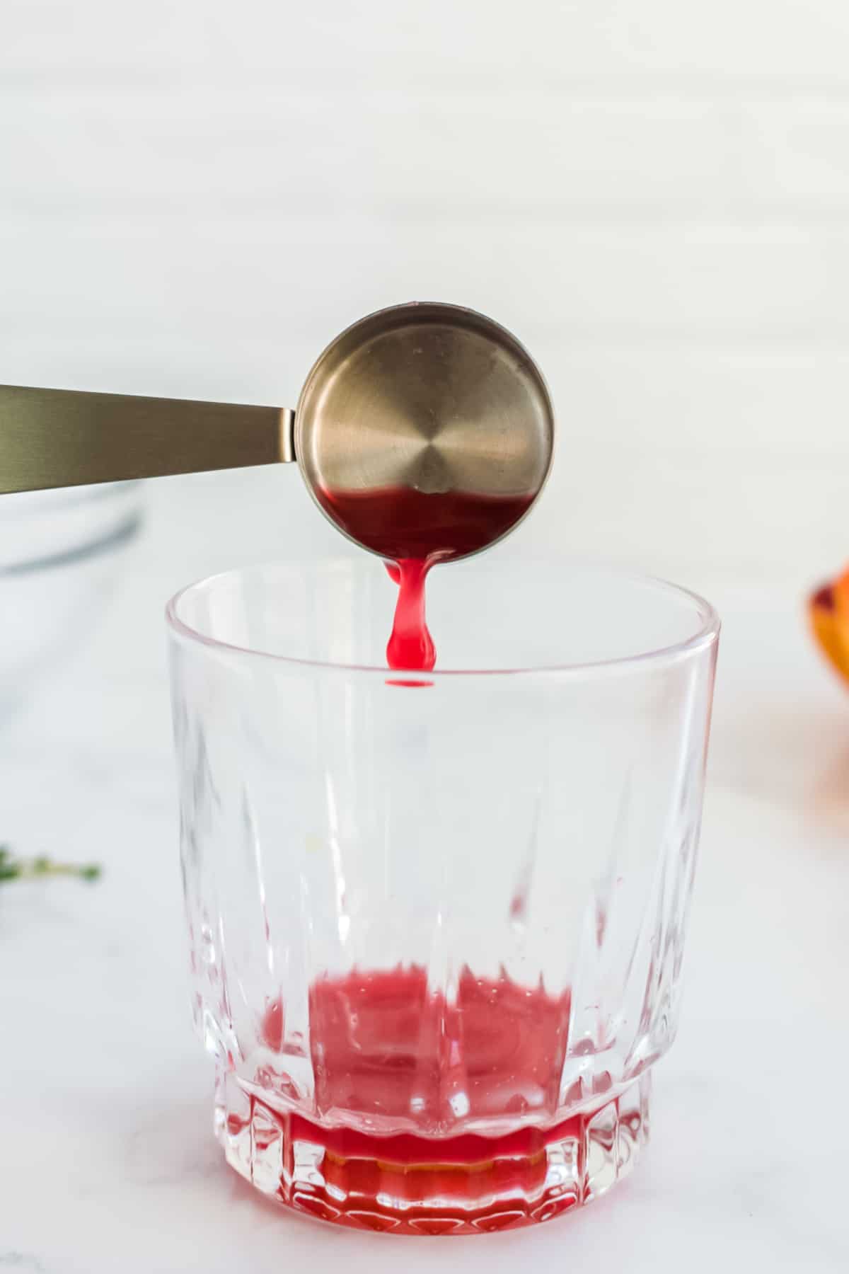 A rocks glass on a marble background with blood orange juice being poured in.