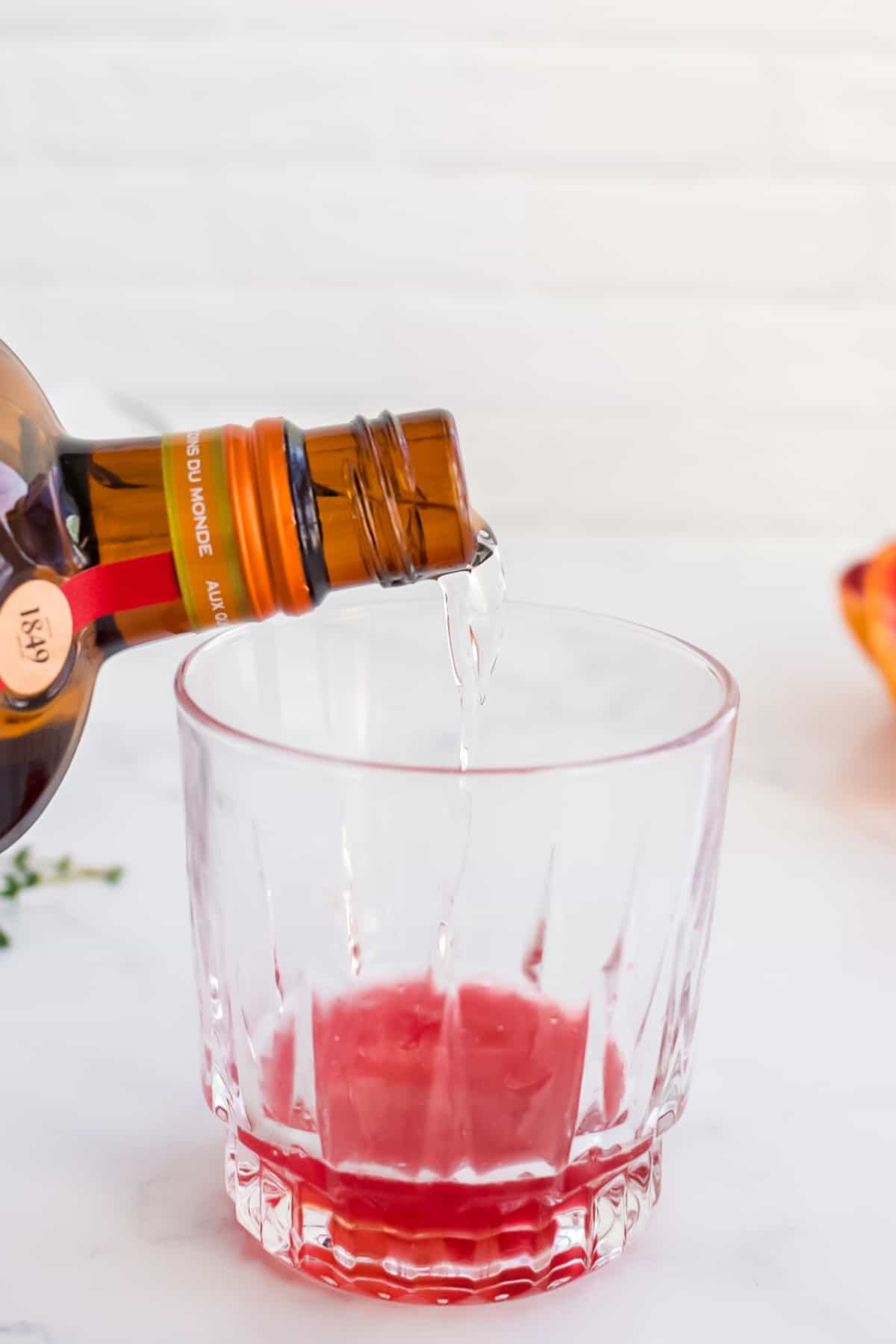 A rocks glass on a marble background with clear alcohol being poured into blood orange juice.