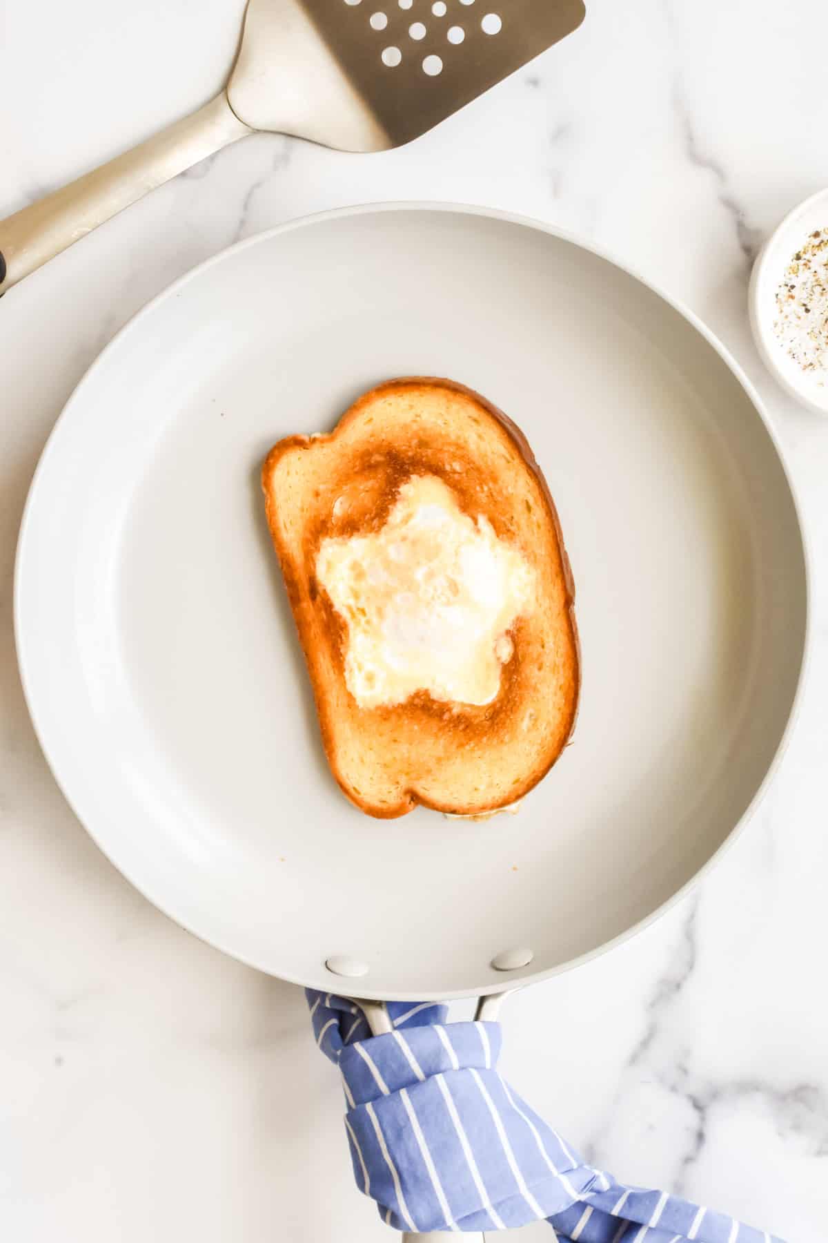 A grey skillet on a marble background. The skillet contains a slice of toasted bread with a cooked egg in a star shaped hole.