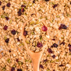 A close up of a wooden spoon with a scoop of maple walnut granola dotted with cranberries and pepitas.