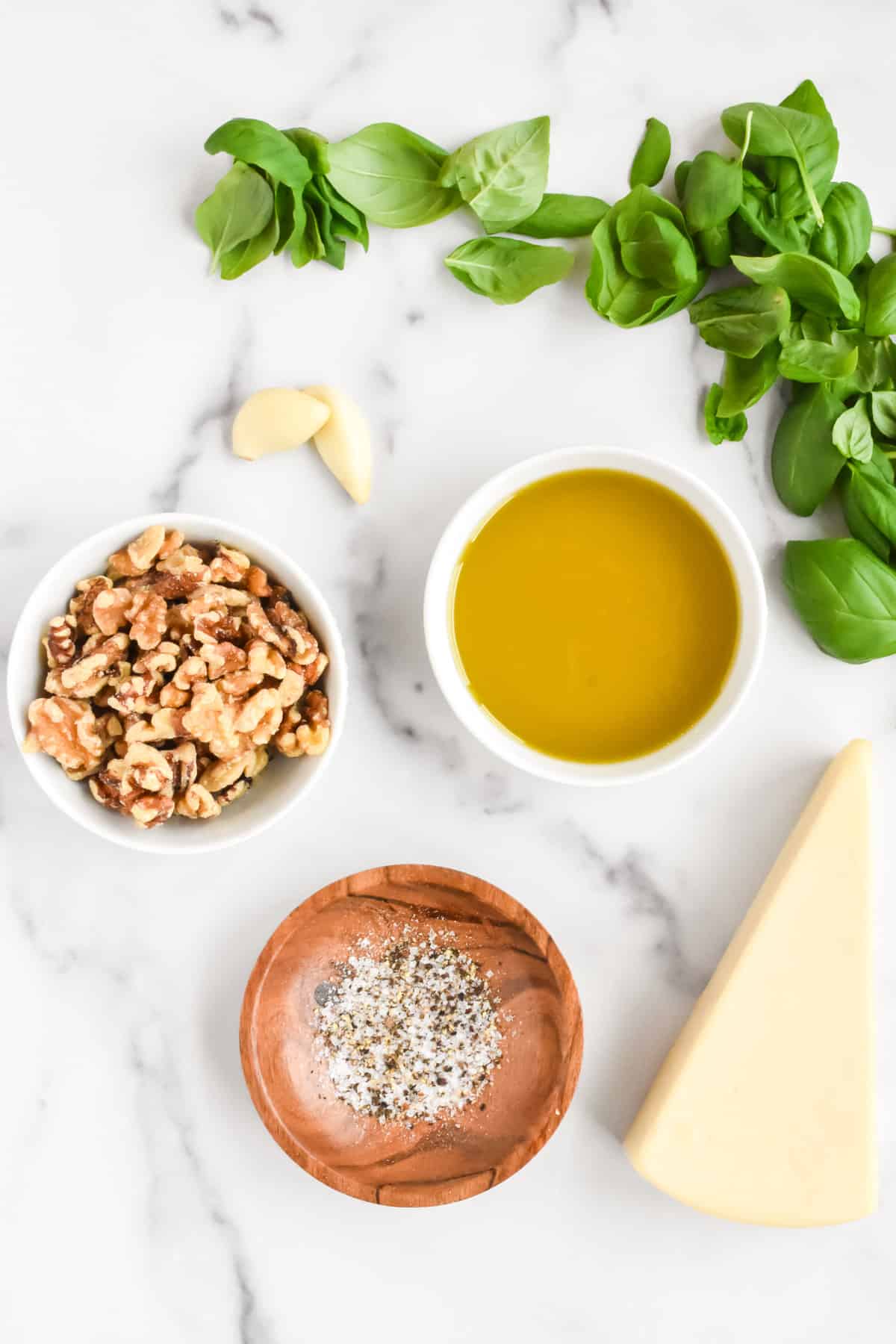 Ingredients for pesto without pine nuts on a marble background, including basil, walnuts, parmesa, olive oil, garlic, salt and pepper.