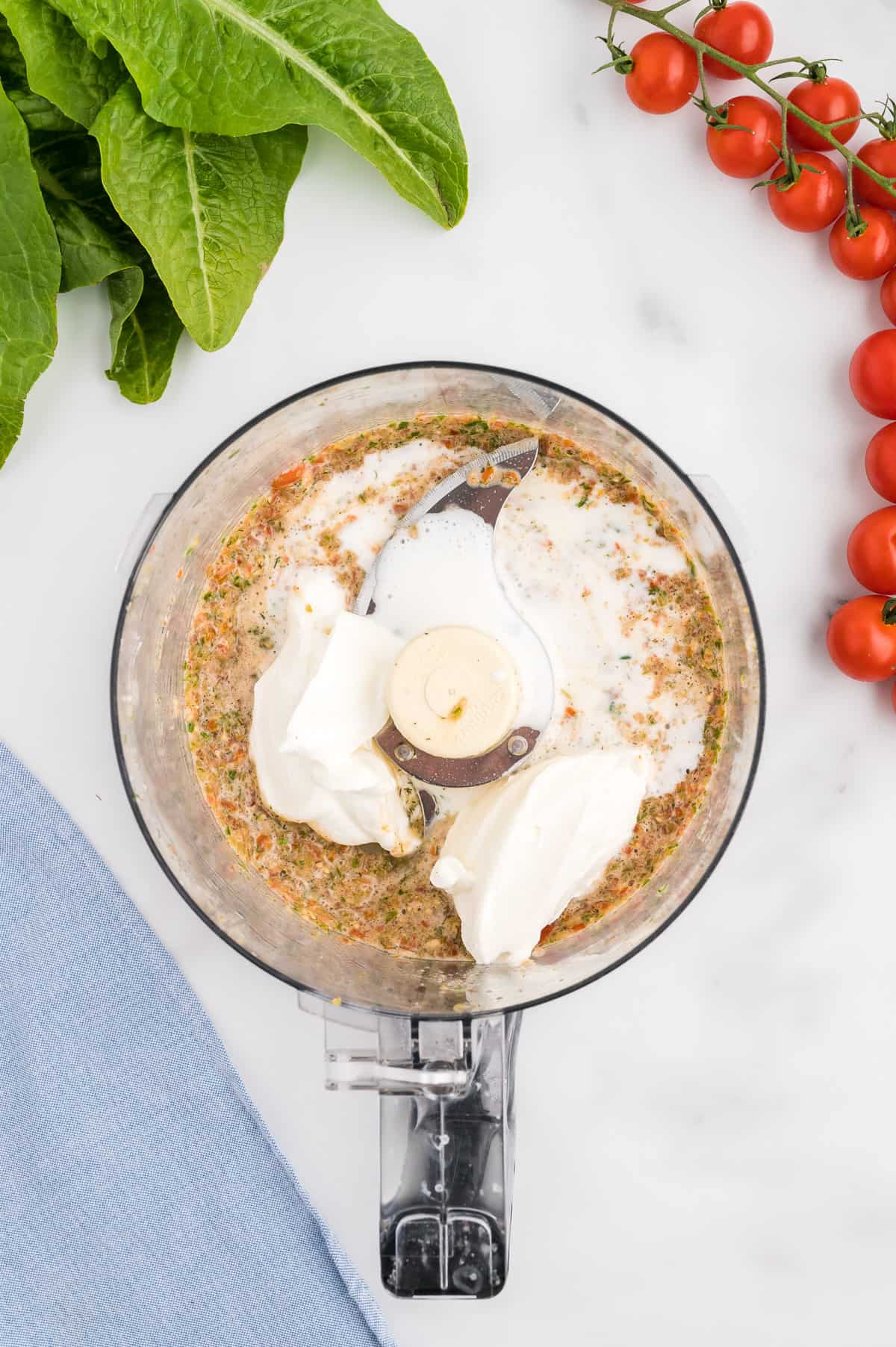 The bowl of a food processor with salsa topped with greek yogurt, sour cream and buttermilk.