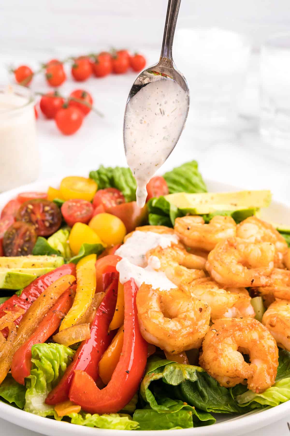 A spoon drizzling salsa ranch dressing onto a shrimp fajita salad.