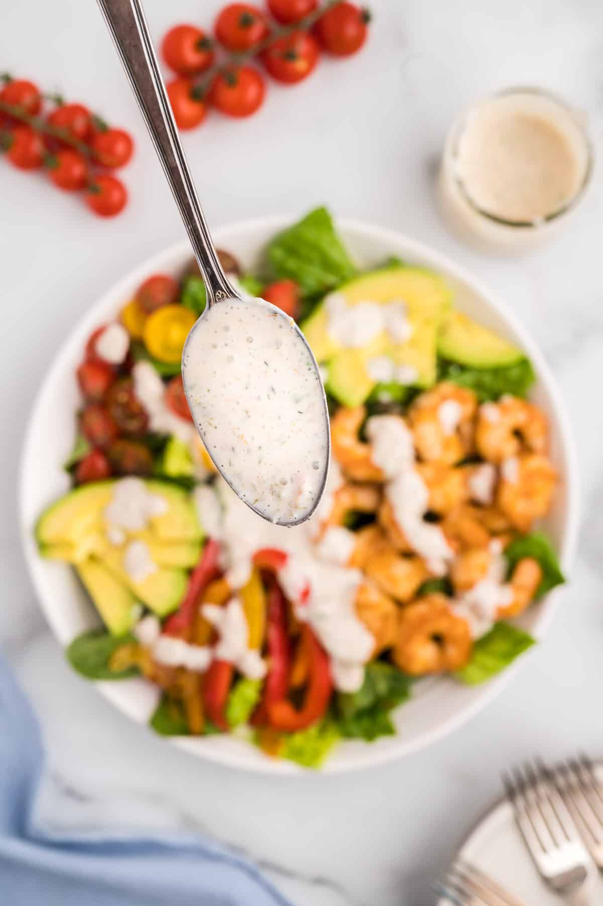 A close up of a spoon with salsa ranch dressing, with a fajita salad blurred in the background.