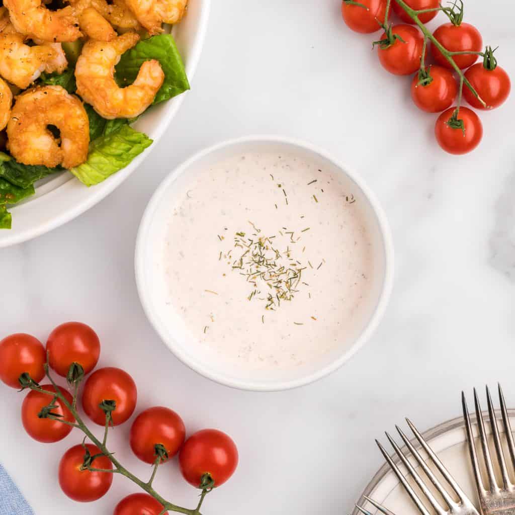 A bowl of salsa ranch dressing, with a shrimp fajita salad and cherry tomatoes off to the side.