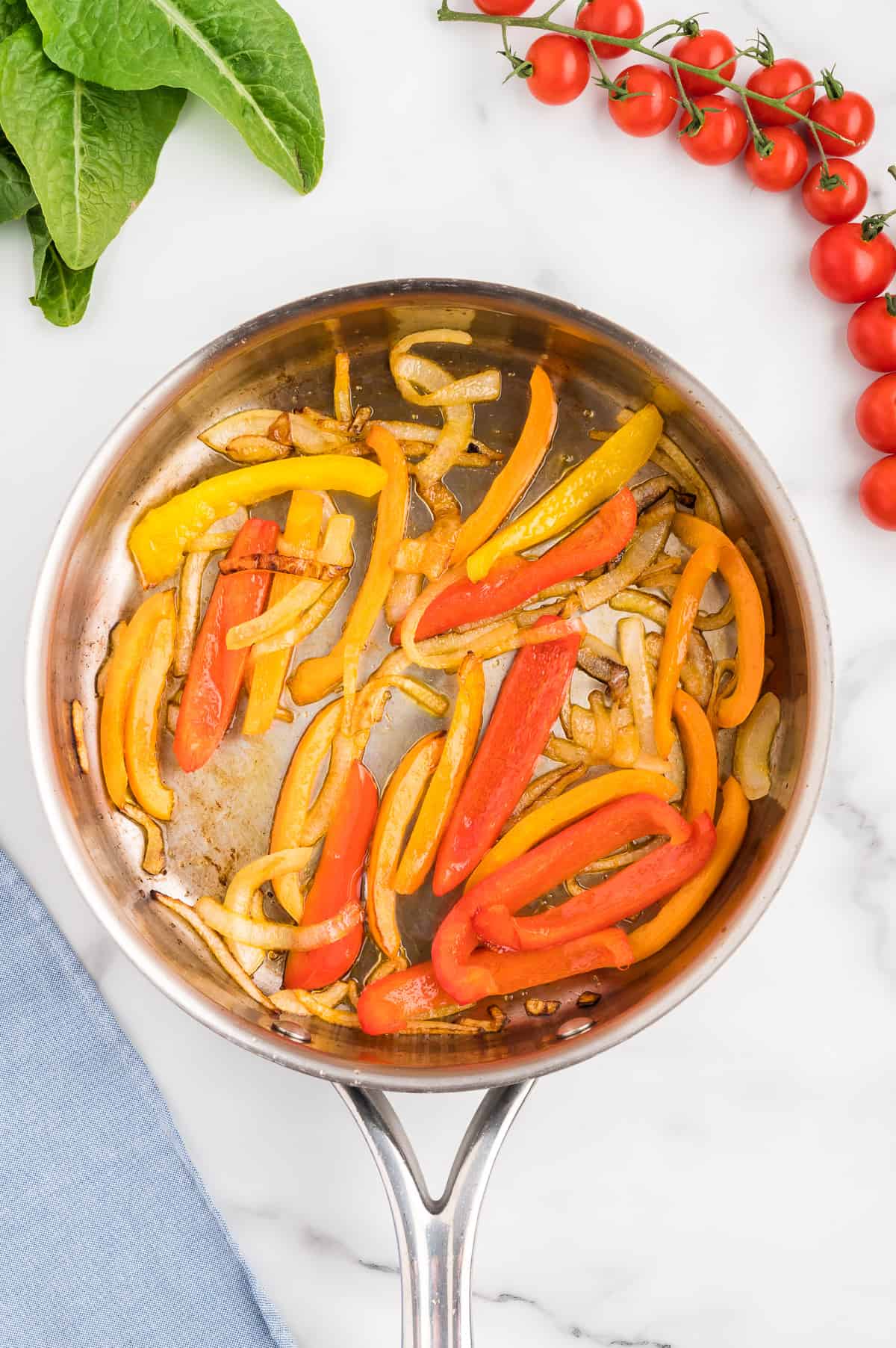 A stainless steel pan with sauteed onions and peppers on a marble background.