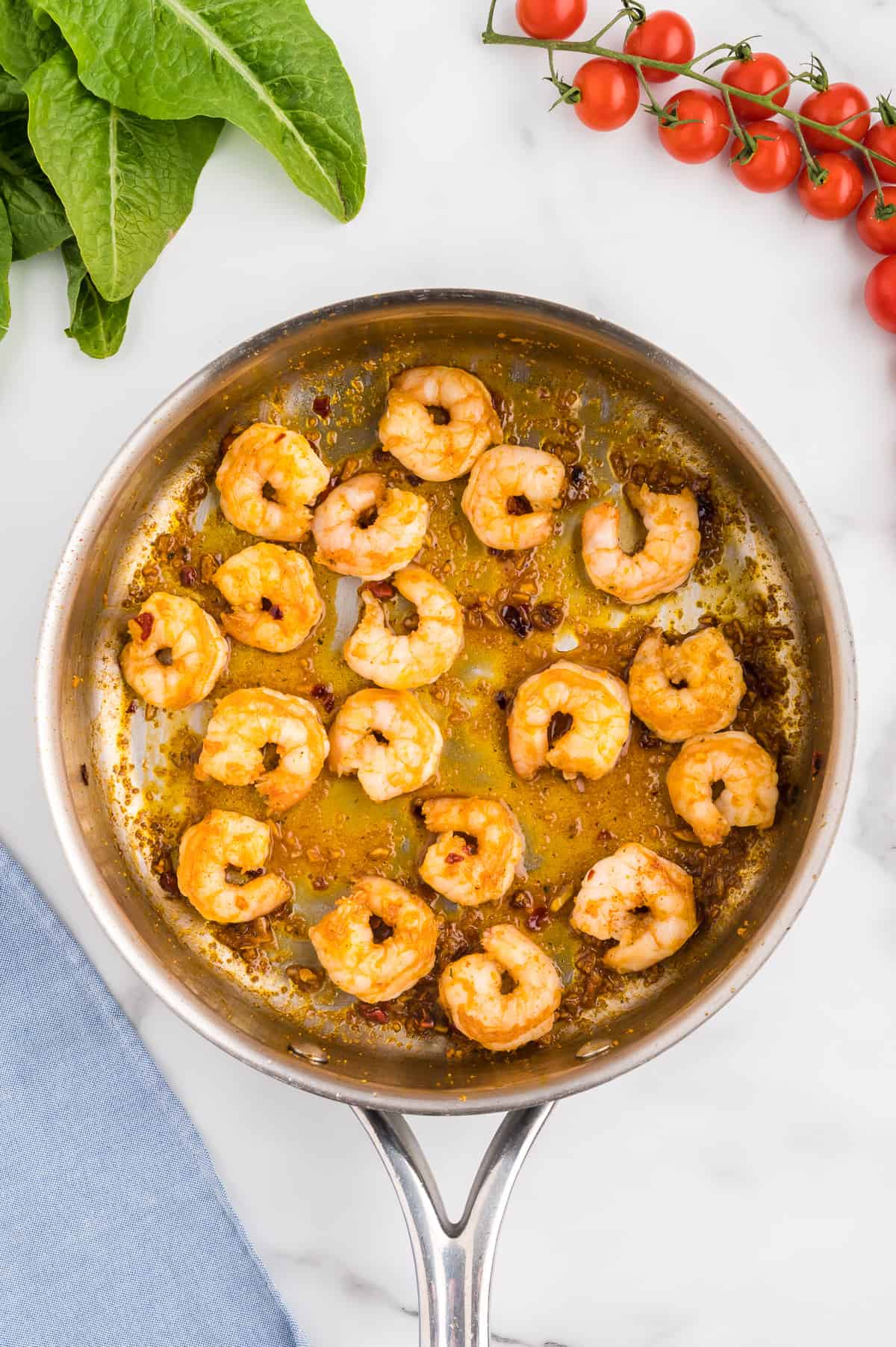 A stainless steel pan with sauteed shrimp in fajita seasoning on a marble background.