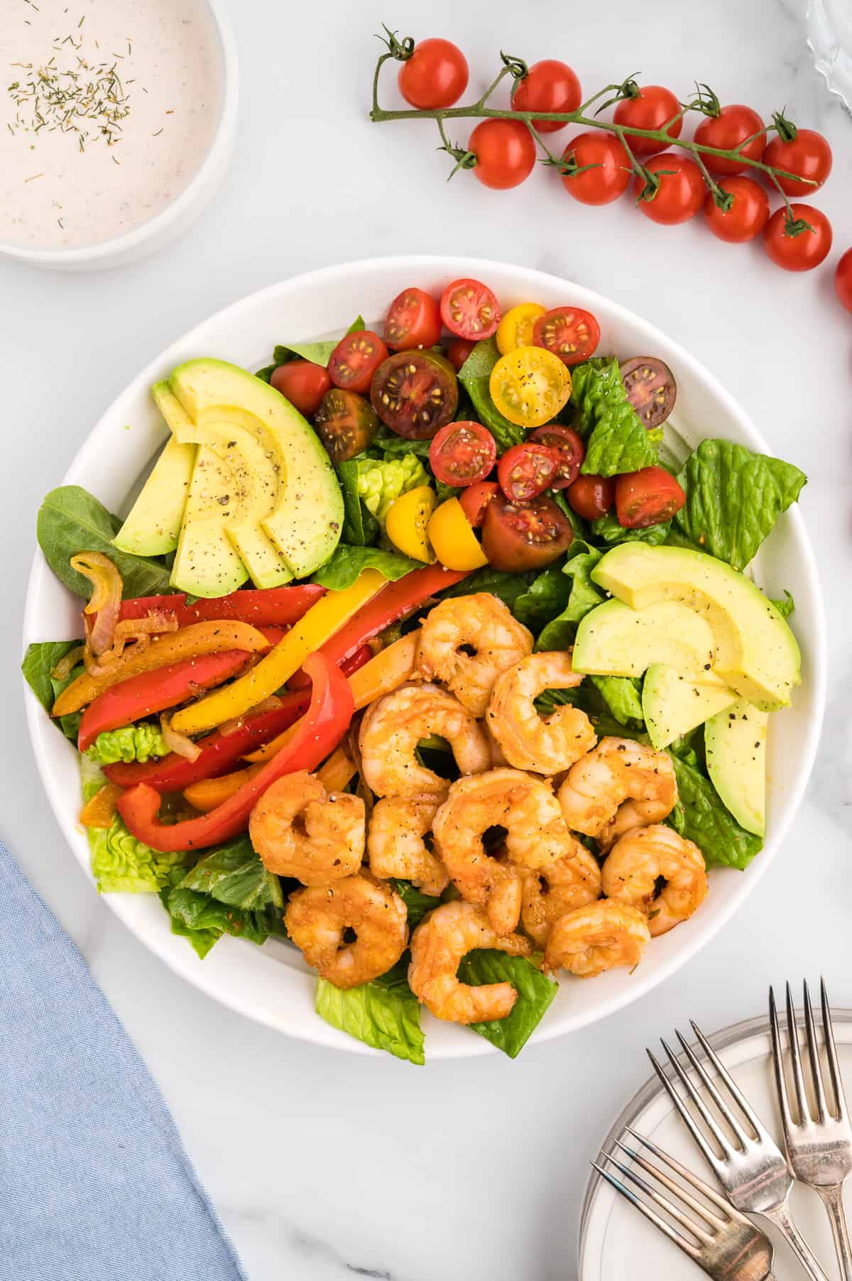 A white bowl with layers of romaine, shrimp, fajita veggies, cherry tomatoes and avocado.