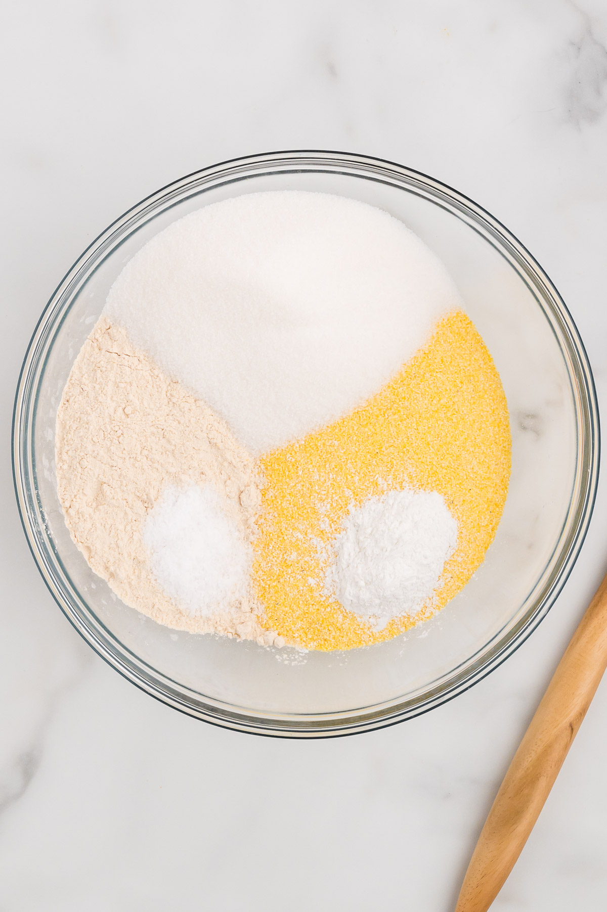 A glass bowl with dry ingredients for cornbread portioned into the bowl but not yet mixed together.