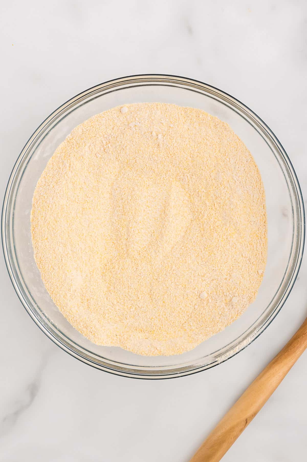 A glass bowl with dry ingredients for cornbread mixed together.