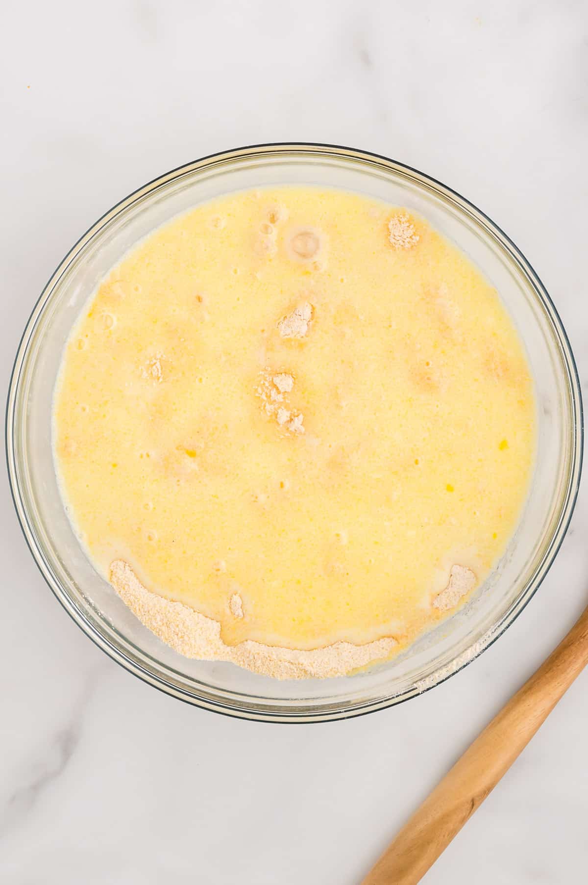 A glass bowl with wet ingredients for cornbread poured on top of dry ingredients.