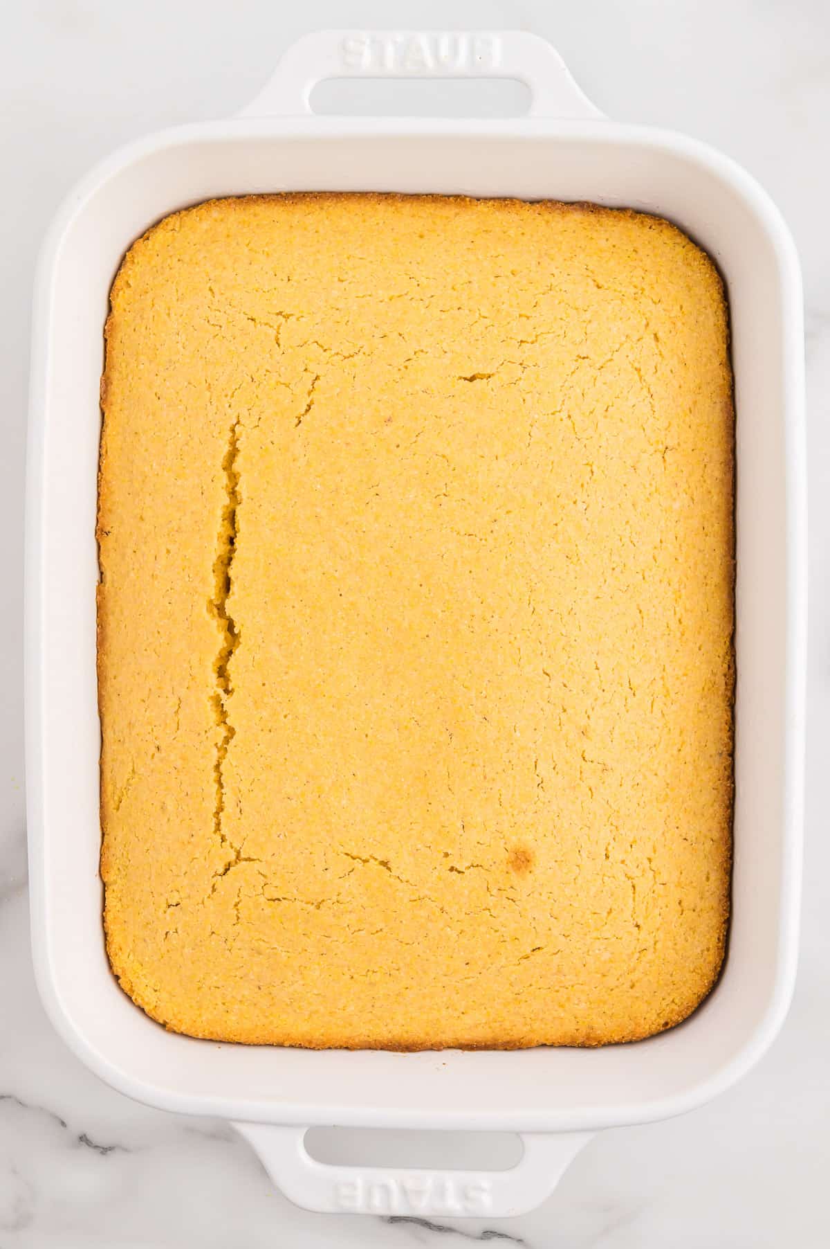 A white baking dish with baked whole grain cornbread on a marble background.