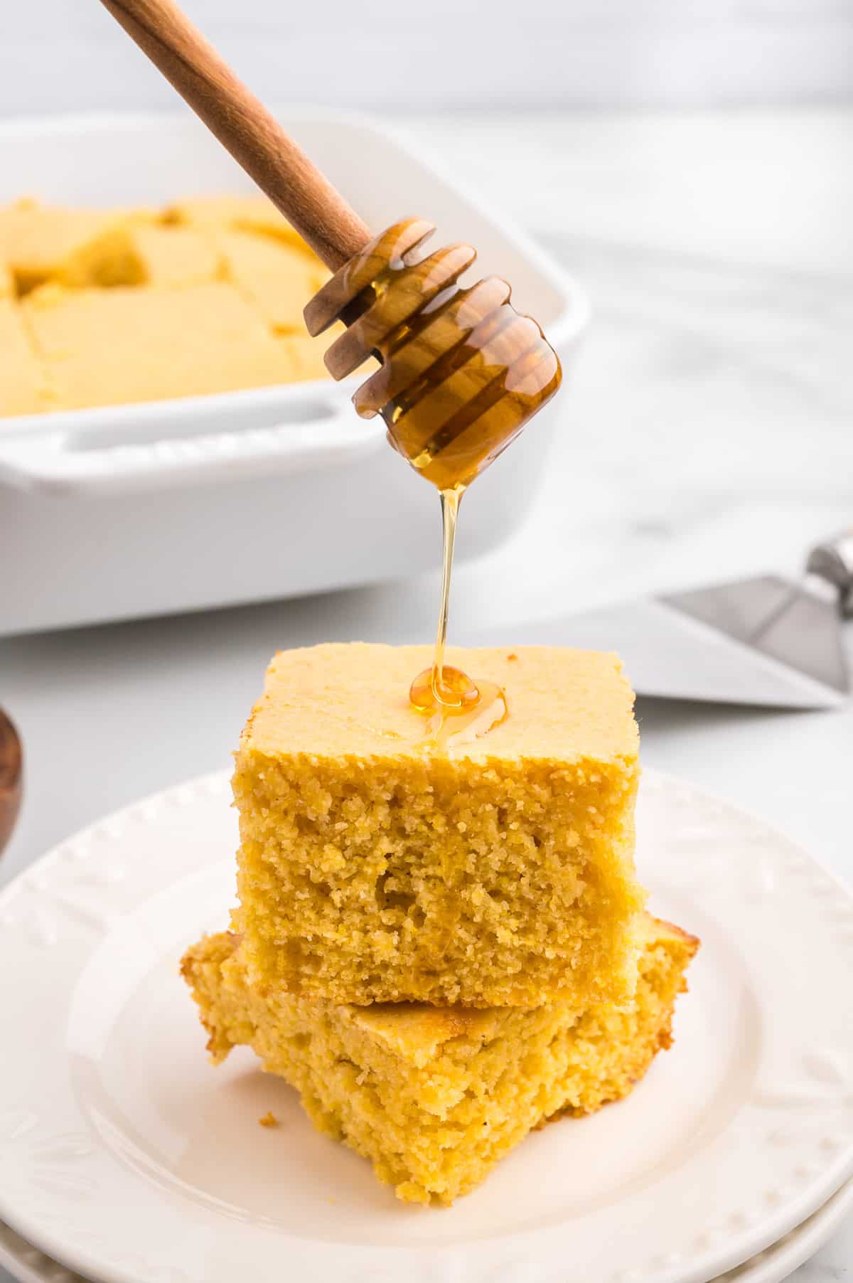 A stack of two slices of cornbread on a white plate, with honey drizzling down onto it from above.