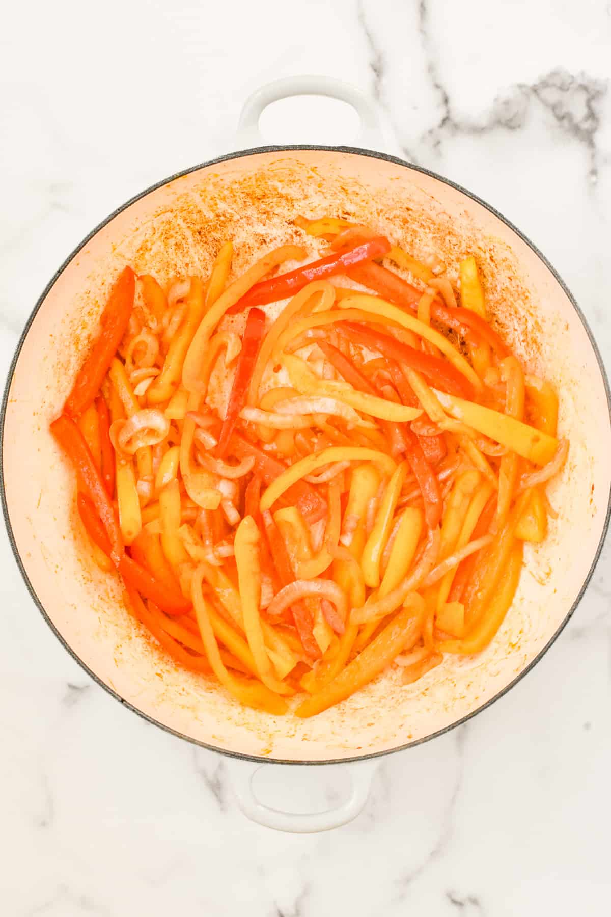 A white skillet on a marble background. The skillet contains sautéed onions and peppers.