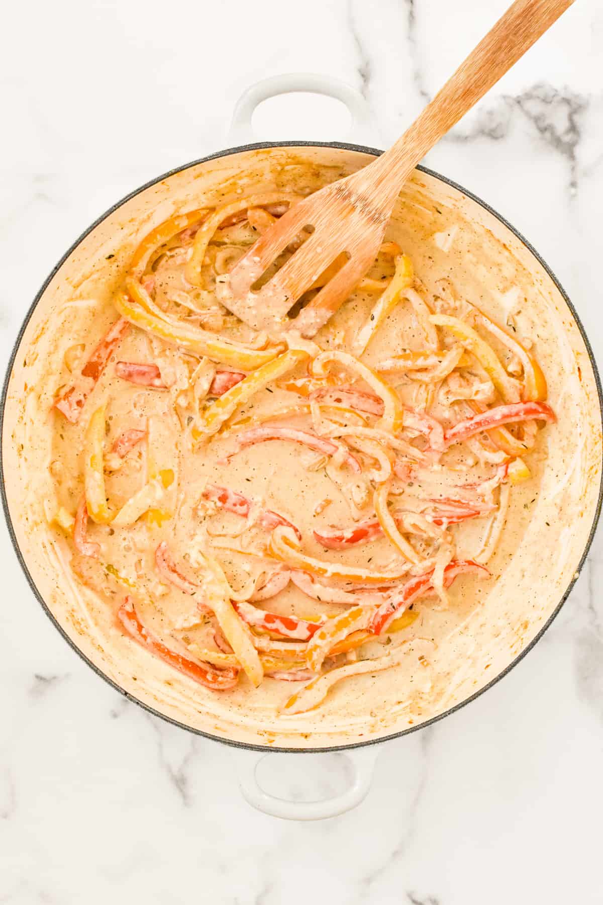 A white skillet on a marble background. The skillet contains jerk alfredo sauce, with peppers and onions mixed in.