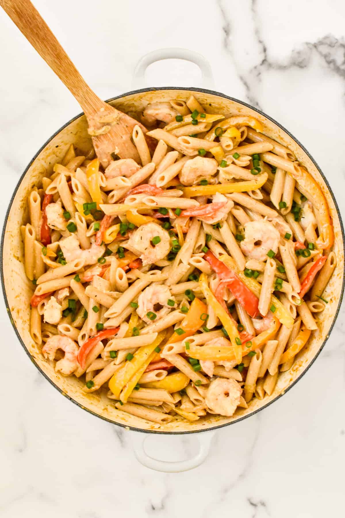 A white skillet on a marble background. The skillet contains rasta pasta with shrimp, dotted with green onions.