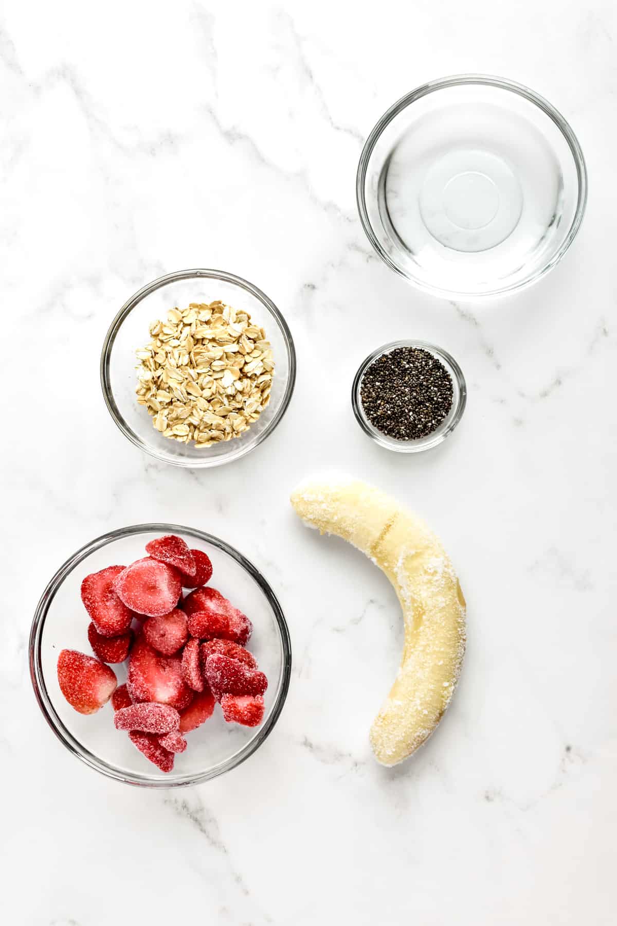 Ingredients for strawberry banana smoothie bowls on a marble background.