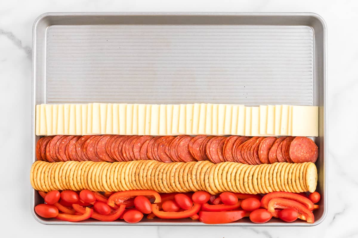 A rimmed sheet pan on a marble background. The sheet pan contains a charcuterie board flag, with 4 alternating red and white stripes. The top half of the sheet pan is empty.