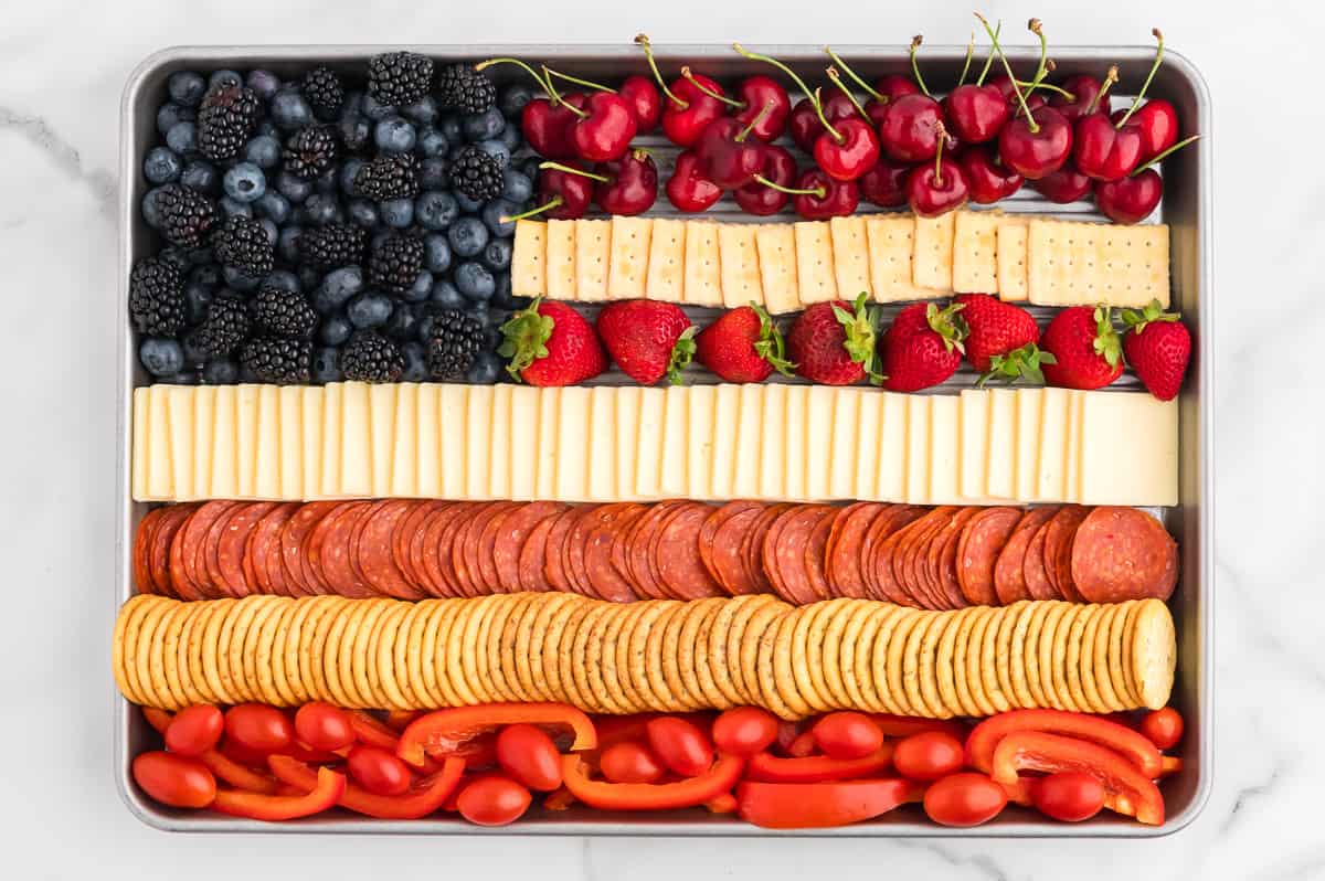 A rimmed sheet pan on a marble background. The sheet pan contains a charcuterie board flag, with 7 alternating red and white stripes and a blue square in the top left corner.