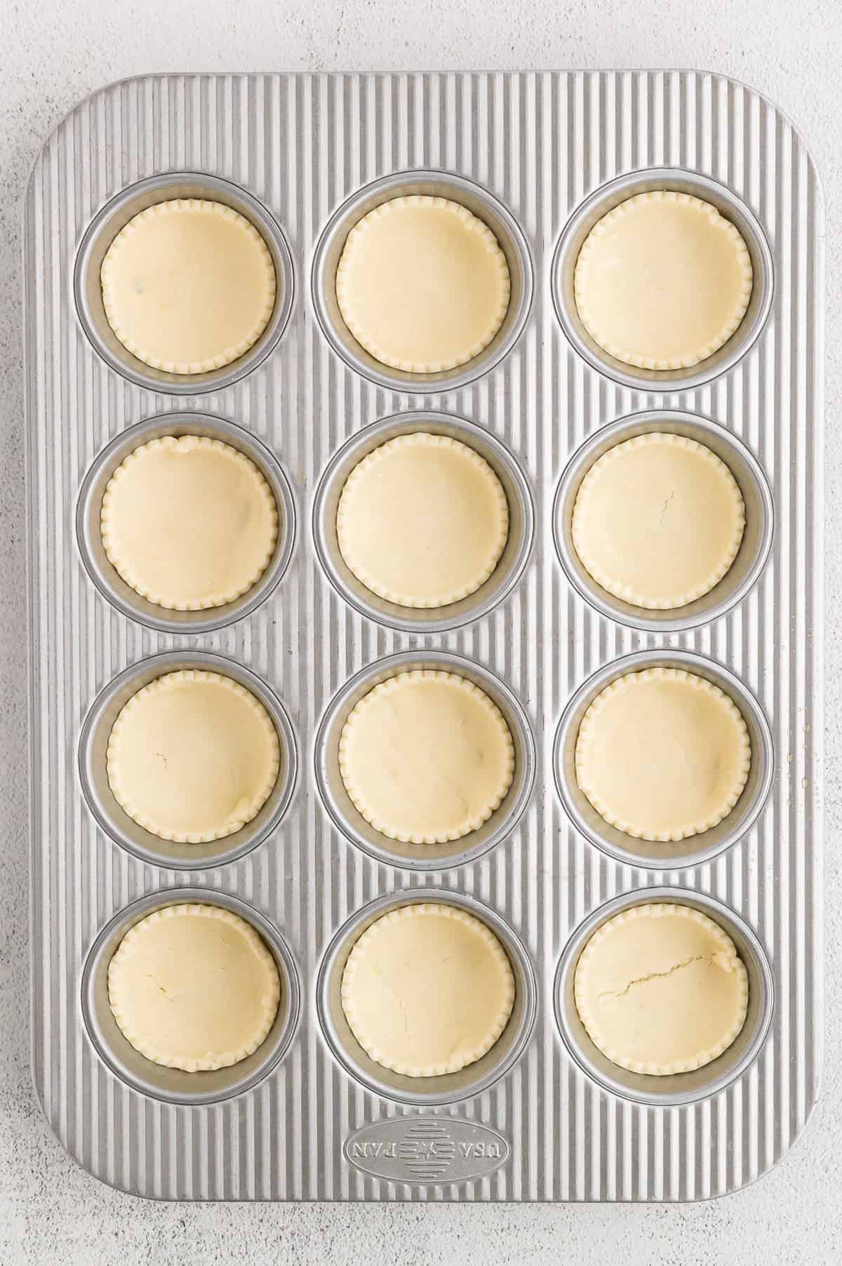 A muffin pan with pie crust in each cup.