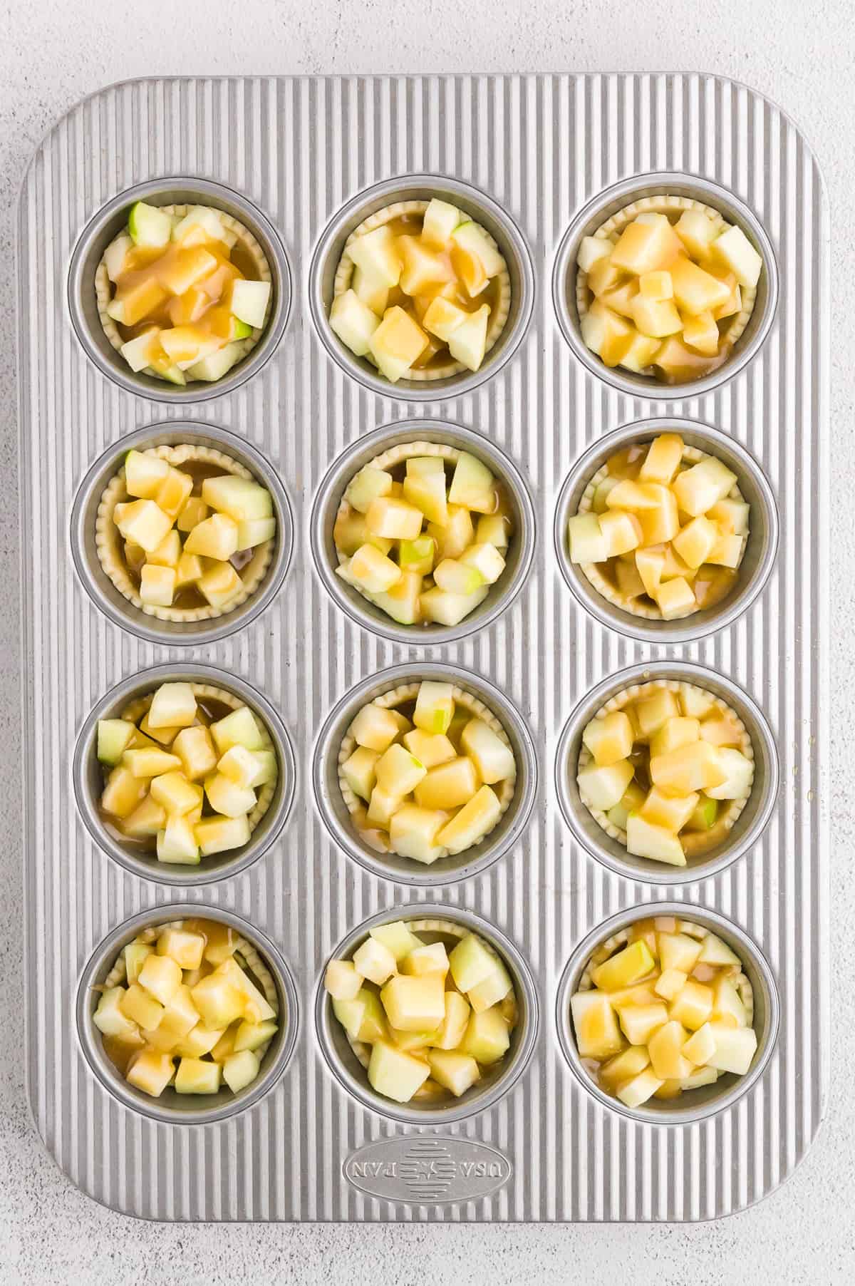 A muffin pan with pie crust, apples and caramel sauce.