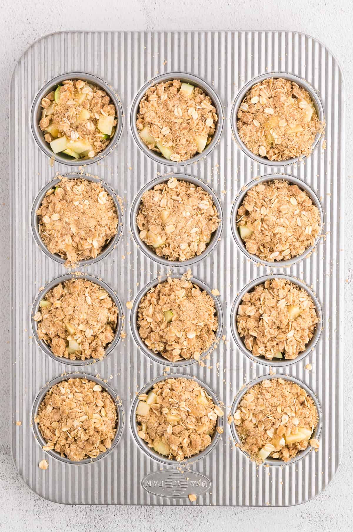 A muffin pan of apple crumble tartlets, not yet baked.