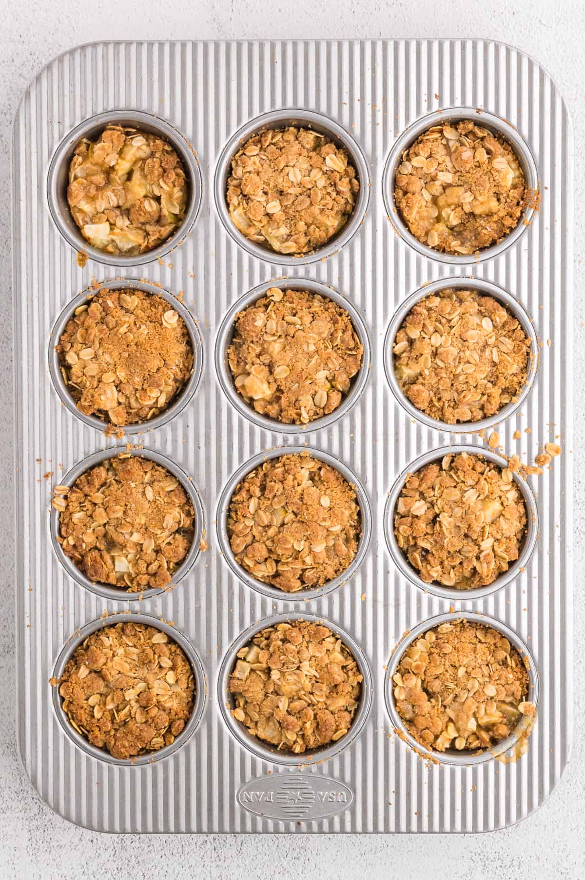 A muffin pan of baked apple crumble tartlets.