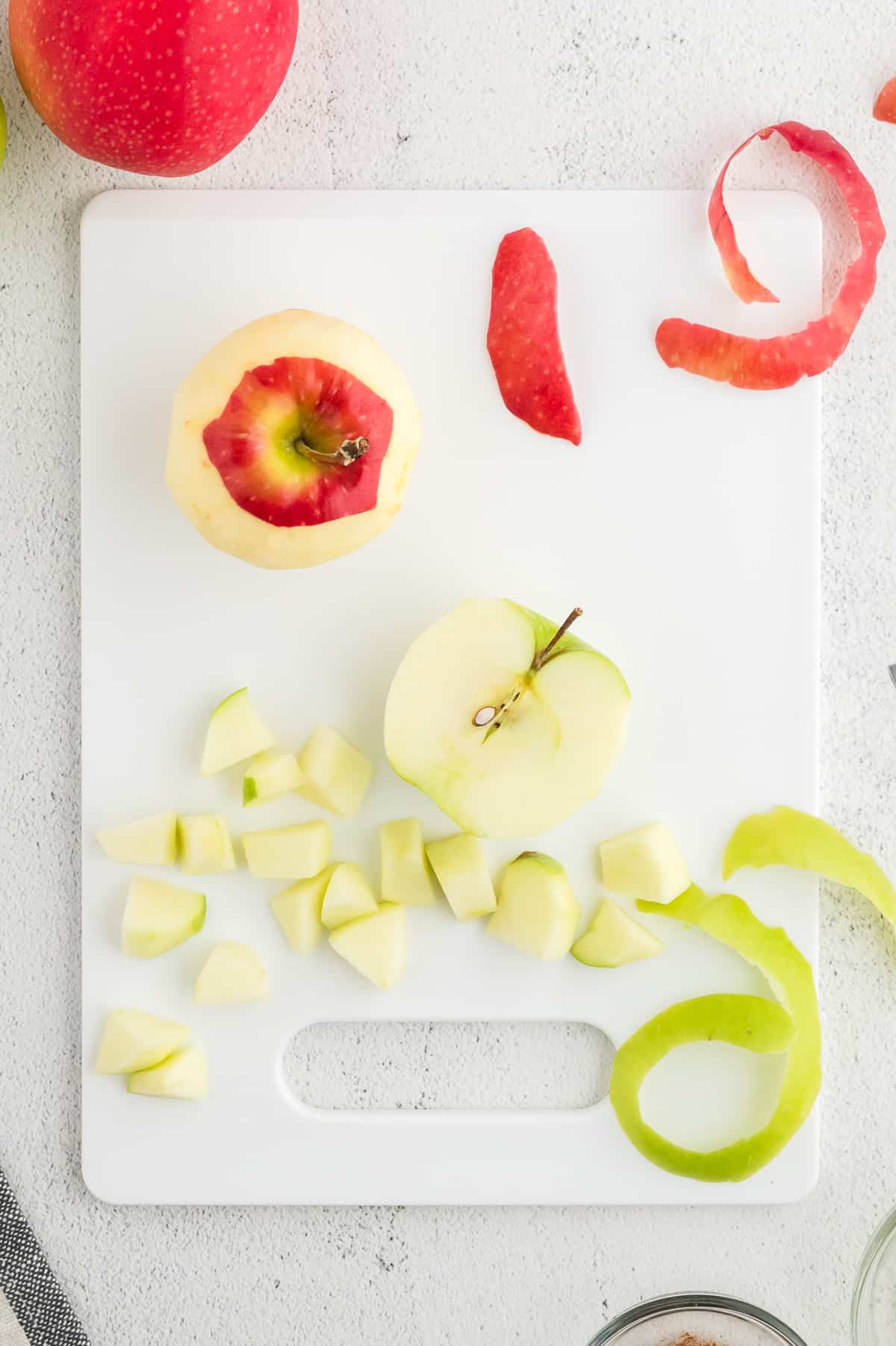 A white cutting board with green and red apples being peeled and diced.