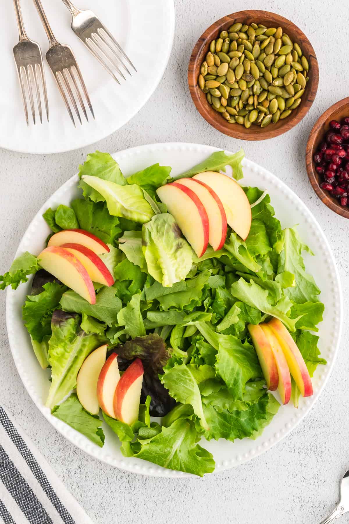 Assembly of the delicata squash salad, showing sliced apples over a bed of lettuce.