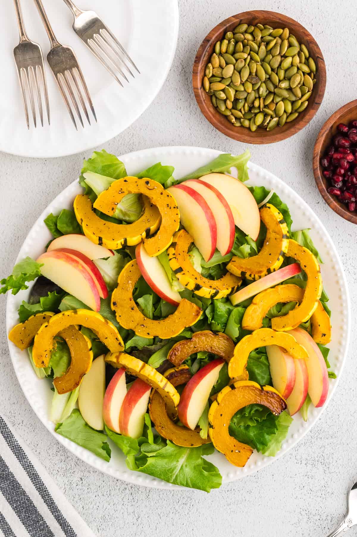 Assembly of the delicata squash salad, showing apples and delicata squash over a bed of lettuce.