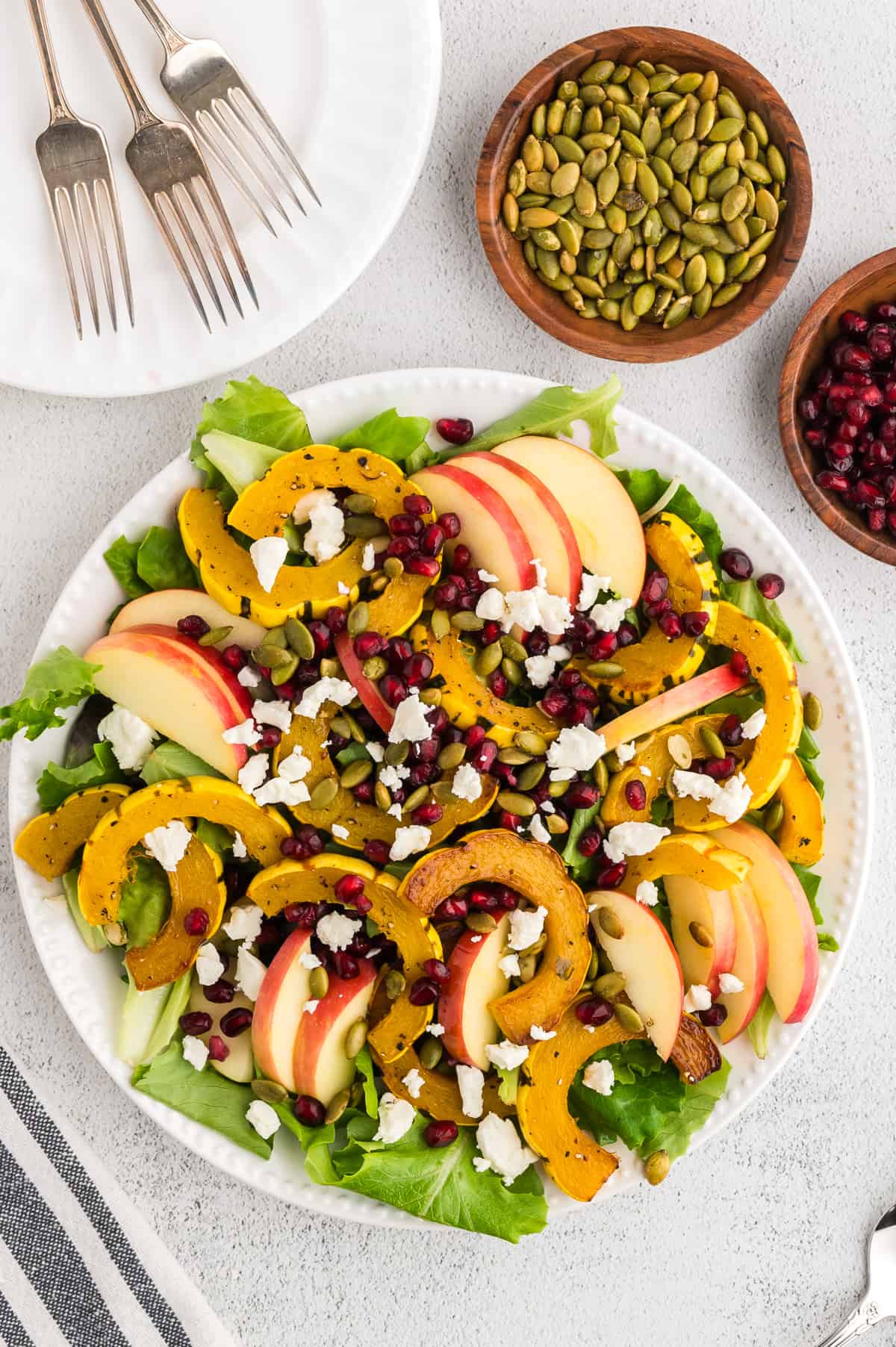 Delicata squash salad on a round plate, with pomegranate arils and pepitas to the side.