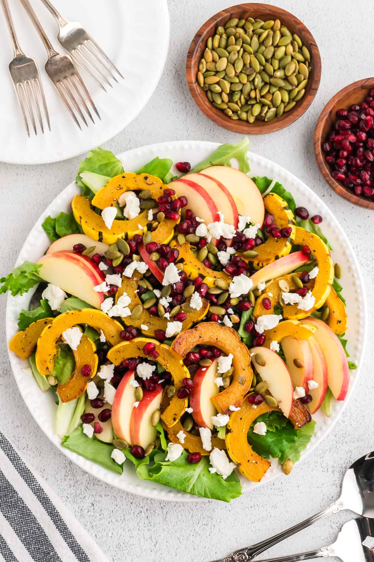 Delicata squash salad on a round plate, with pomegranate arils and pepitas to the side.