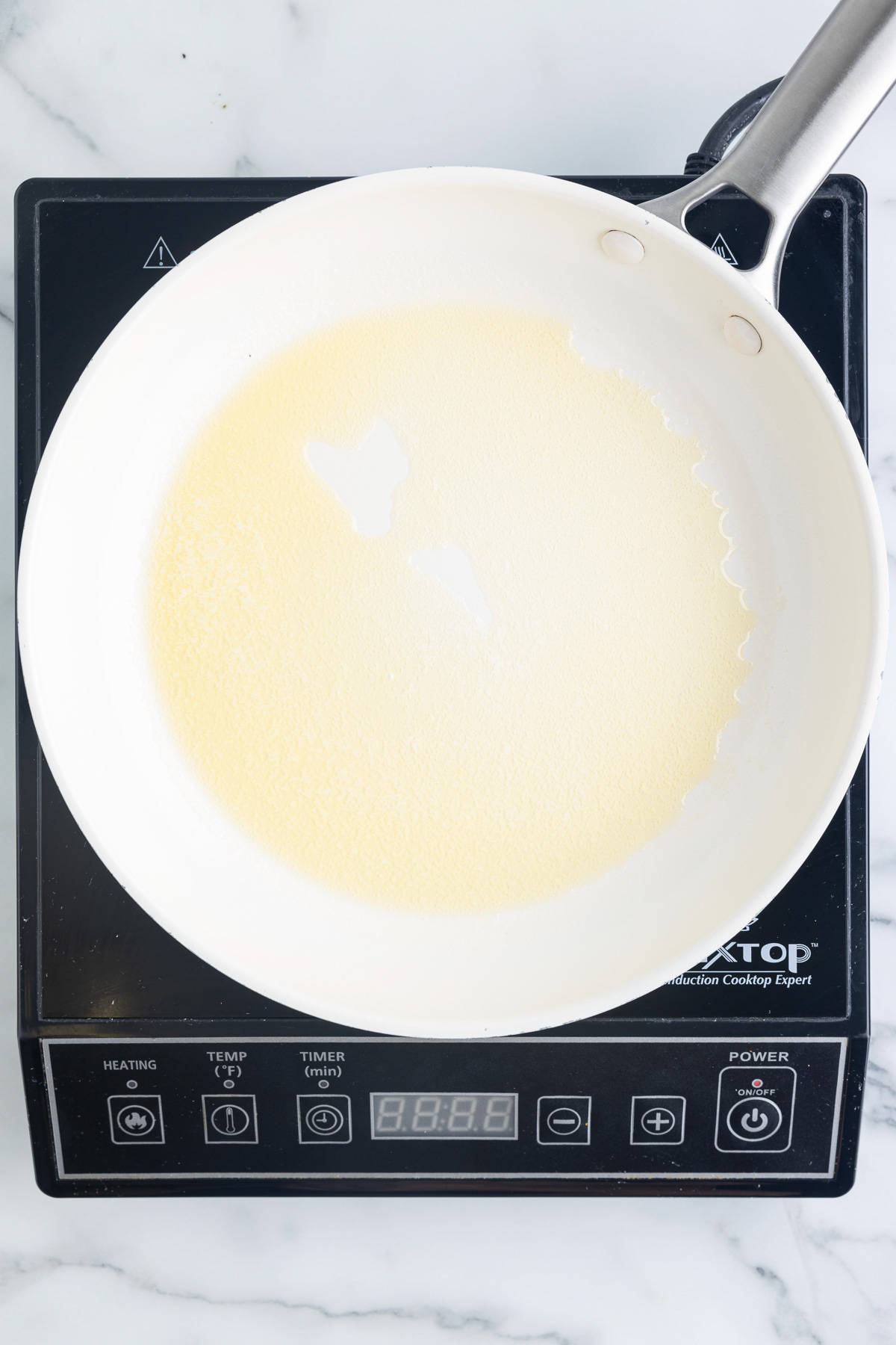 A white skillet on a black cooktop sitting on a marble background. The skillet has melted butter in it.