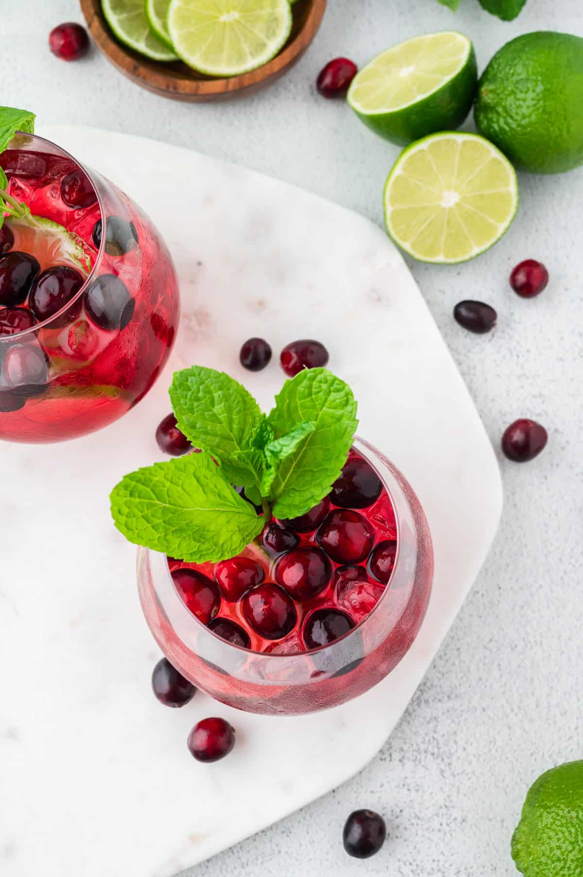 A top down view of a 2 vodka cranberry spritzers, garnished with lime, mint and cranberry.