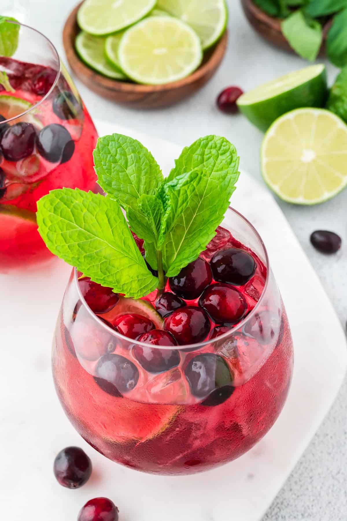 A close-up side view of a vodka cranberry spritzer, garnished with lime, mint and cranberry.