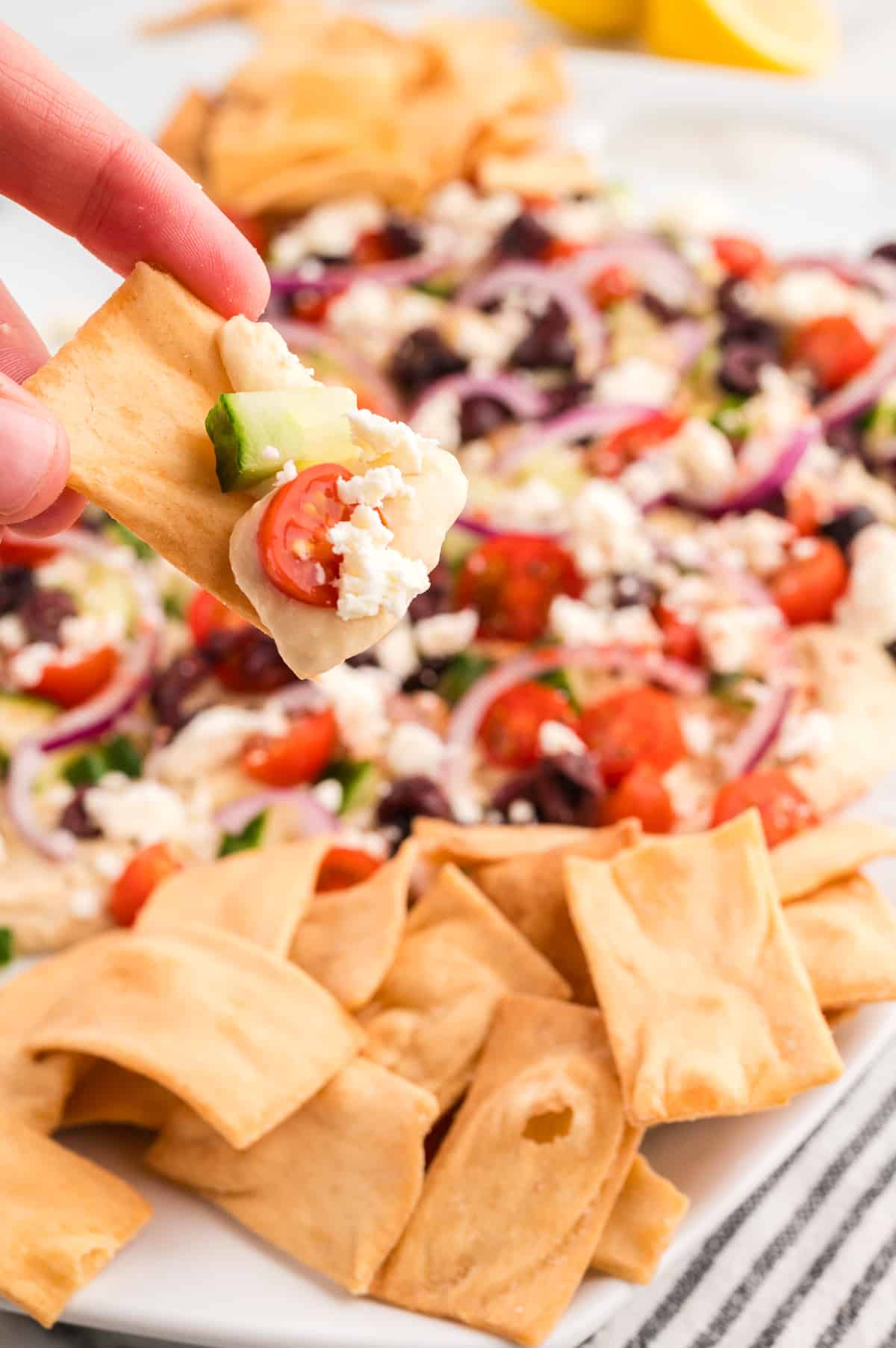 A hand holding a pita chip with loaded hummus.